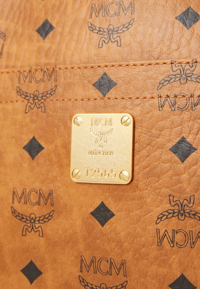 Brown leather handbag featuring a gold metal plate with embossed logo, diamond patterns, and black winged designs throughout.