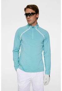 Ljusblå långärmad golftröja med halvdraget krage, med vit accentstickning. Bärs tillsammans med vita byxor och en handskar.