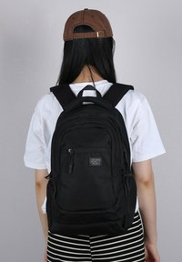 Zaino nero con molteplici scomparti con zip, spallacci imbottiti e una maniglia superiore. Il materiale sembra resistente e testurizzato.