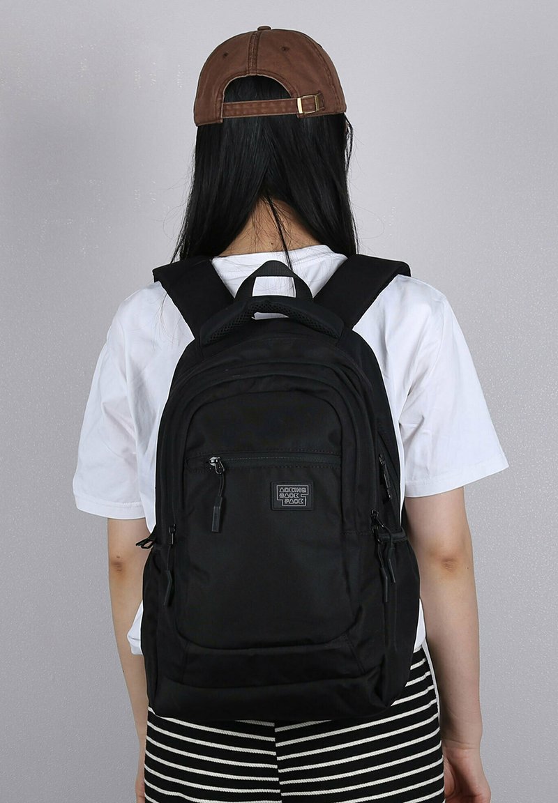 Zaino nero con molteplici scomparti con zip, spallacci imbottiti e una maniglia superiore. Il materiale sembra resistente e testurizzato.