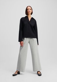Black cropped pullover with a collar, paired with wide-leg light gray trousers and black flats featuring white polka dots.