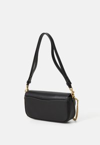 Black leather shoulder bag with curved flap, gold chain and adjustable double strap with white stitching on a white background.