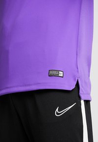 Purple short-sleeve sports jersey with a mesh texture, featuring a "AUTHENTIC FOOTBALL" tag at the hem and contrast black shorts with white accents.
