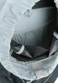 Interno di uno zaino grigio con una base nera tessurizzata, parte superiore con cordino elastico e spallacci grigi. Presenta un rivestimento liscio e diversi scomparti.