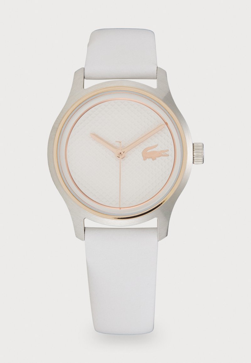 Montre avec bracelet en caoutchouc blanc, cadran blanc texturé, accents en or rose et un petit logo de crocodile. Boîtier en acier inoxydable, design minimaliste.