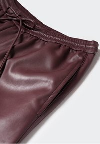 Pantalon en cuir bordeaux avec taille élastique, fermeture à cordon et poches latérales sur un fond uni clair.