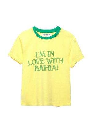 Sárga pamut póló zöld bordás környakrészsel. Az "IM IN LOVE WITH BAHIA!" szöveg zöld, vastag, sans-serif betűtípussal szerepel rajta.