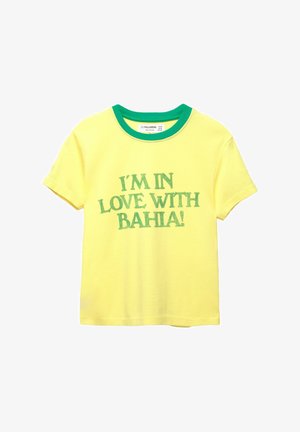 Sárga pamut póló zöld bordás környakrészsel. Az "IM IN LOVE WITH BAHIA!" szöveg zöld, vastag, sans-serif betűtípussal szerepel rajta.