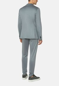 Grijze suit gemaakt van structuurstof, met een getailleerde pasvorm, enkele split en gecombineerd met grijze sneakers. Subtiele accenten op de knopen.