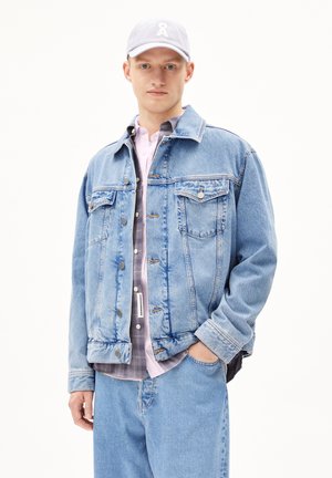 Light blue denim jacket with two chest pockets, silver buttons, and a relaxed fit, layered over a gray button-up and light pink shirt.
