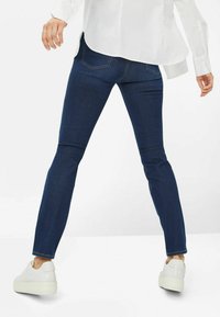 Jean bleu foncé à coupe slim, avec des poches arrière et une texture de tissu lisse, accompagnés de baskets à plateforme blanches.