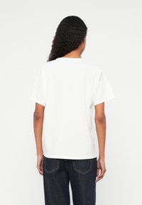 Balts kokvilnas T-krekls ar brīvu piegriezumu, apaļu izgriezumu un īsām piedurknēm. Vienkāršs dizains bez rakstiem vai izcēlumiem, redzama no aizmugures.