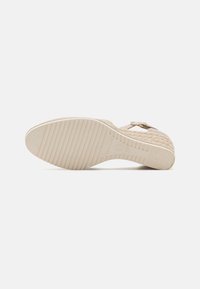 Sandalia de cuña beige que presenta un upper de tela texturizada, hebilla de metal ajustable y suela de goma estriada para mayor agarre.