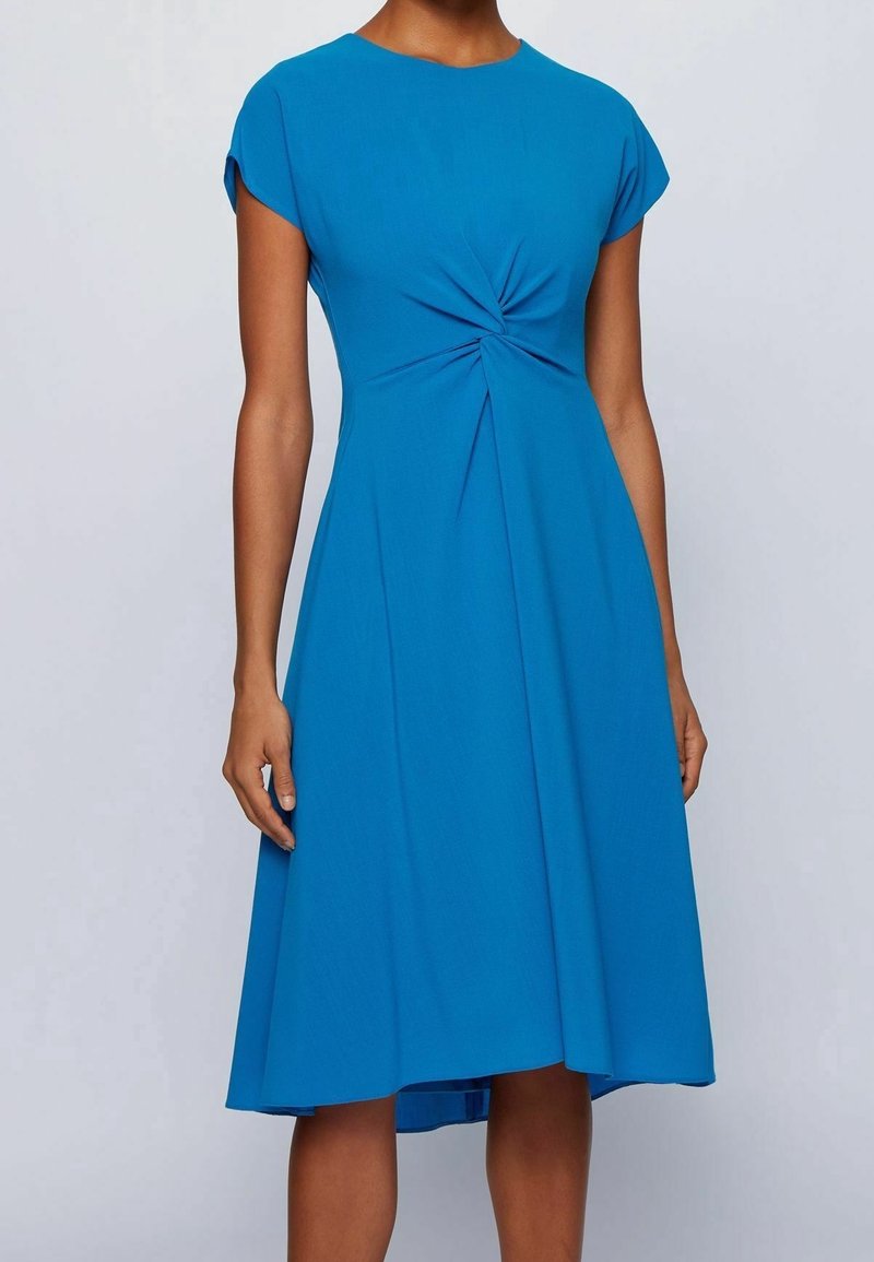 Robe bleue à manches courtes avec un détail twist à la taille, jupe fluide et texture lisse en tissu léger.