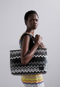 Crna i bijela tote torba s uzorkom chevron, glatke teksture, pravokutnog oblika s malim logotipom na prednjoj strani.