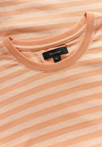 Peach-colored T-shirt featuring horizontal white stripes, round neckline, short sleeves, and a black label with the brand name and size.