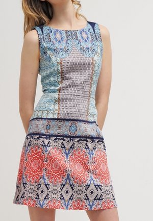 Mouwloze jurk met een getailleerde lijfje en een uitlopende rok. Bevat blauwe en beige geometrische patronen, met rode bloemaccenten aan de zoom.