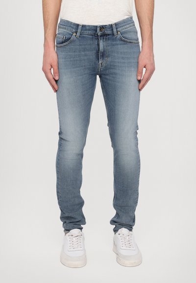 Jeans in denim blu con una vestibilità slim, caratterizzati da un lavaggio sbiadito, cinque tasche e una chiusura zip. Abbinati a sneakers bianche.