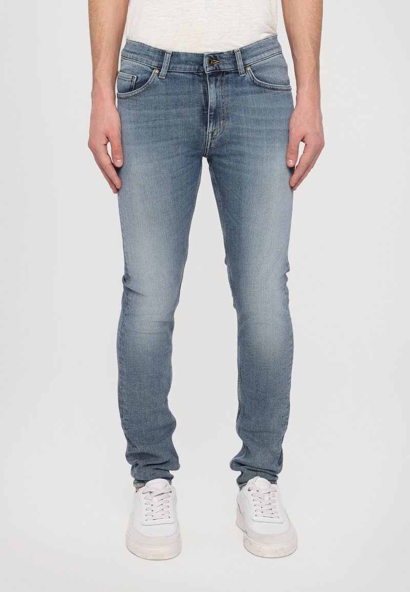 Zila denim auduma bikses ar šauru piegriezumu, ar izbalējušu mazgāšanu, piecām kabatām un rāvējslēdzēju. Stilizētas ar baltām kedām.