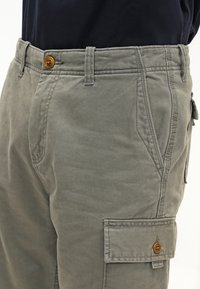 Pantalones cargo en gris claro con cierre de botón, bolsillos laterales y detalles cosidos, fabricados en un material de algodón resistente.