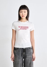 Bílý tričko s krátkým rukávem s červeným potiskem "tommy jeans" na hrudi, vyrobené z bavlny, s klasickým střihem a kulatým výstřihem.