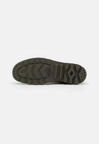 Suela de zapato de color verde oliva, con una superficie texturizada, canales profundos para tracción y múltiples patrones elevados.
