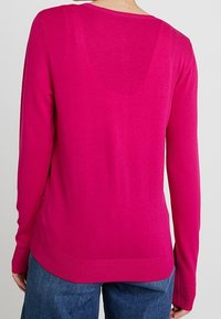 Fuksianvärinen pitkähiha neulepaita, jossa on pyöreä pääntie, resorireunus ja sileä pinta. Takakuvassa näkyy hieman pidennetty takahelma.