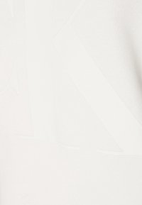 Vit tyg t-shirt med en stor, subtil präglad "K" design. Texturen ser slät ut med en lätt och andningsbar struktur.