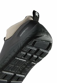 Podeszwa szaro-czarnych butów z głębokim wzorem bieżnika oraz logo "reima TEC", z widoczną tkaninową pętlą oznaczoną literą "R" na pięcie.