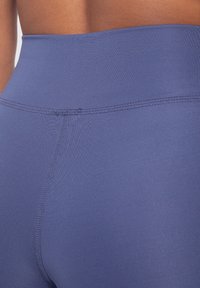 Close-up van een persoon die hoge, naadloze, blauwe sportleggings draagt, met zichtbare details van de achter- en zijnaad.