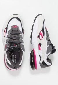 Sneaker a rete grigie e bianche con dettagli rosa, dotate di linguetta imbottita, sistema di allacciatura e un'unità di ammortizzazione ad aria visibile nella suola.