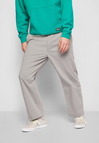 Světle šedé volné kalhoty spárované s tyrkysovou mikinou s kapucí a botami s barevným vzorem. Žádné viditelné doplňky ani výrazné vzory.