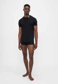 Schwarz, kurzärmliges T-Shirt in körperbetontem Design, kombiniert mit schwarzen Boxershorts. Das Material wirkt glatt, ohne sichtbare Muster oder Akzente.