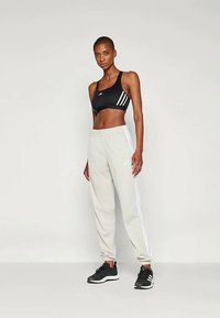 Sutiã desportivo preto com riscas brancas, calças de treino cinzentas claras com riscas laterais brancas e ténis pretos de atletismo. Tecido suave, design ajustado.