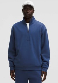 Felpa blu con zip a quarti, colletto alto, texture morbida e orlo a costine, abbinata a pantaloni blu coordinati.