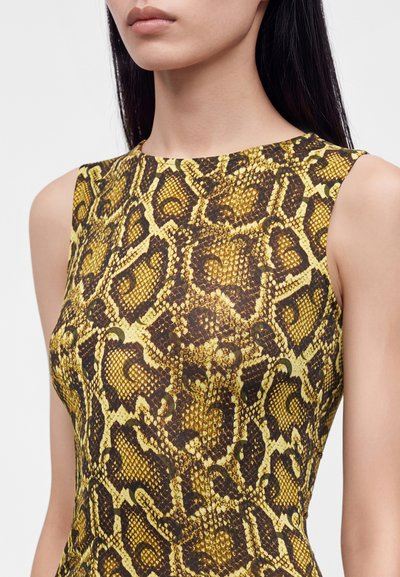 Femme portant un haut sans manches jaune et marron à imprimé serpent, avec un col rond et des épaules droites.