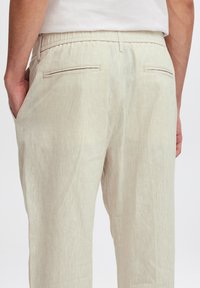 Helle beigen Leinenhosen mit einem entspannten Schnitt, elastischem Bund und zwei Gesäßtaschen mit subtilen Nähten.