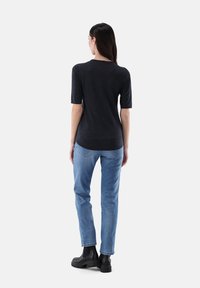 Dunkelgraues Kurzarmtop mit abgerundetem Saum, kombiniert mit hellblauen Jeans und schwarzen Ankle Boots. Glatte Textur, lässige Passform.