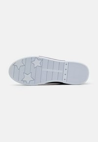 Schuhsohle mit Sternmustern, strukturiertem Grip und "Tommy Hilfiger"-Markierung auf weißem Hintergrund.