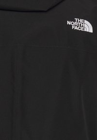 Veste noire avec un logo The North Face brodé en blanc sur la partie supérieure gauche de la poitrine.