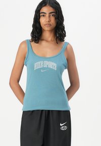 Μπλε βαμβακερό αμάνικο μπλουζάκι με τύπωμα "NIKE SPORTS" και μικρό λογότυπο Nike. Διαθέτει φαρδιές τιράντες και εφαρμοστή γραμμή, συμπληρωμένο με μαύρο παντελόνι.