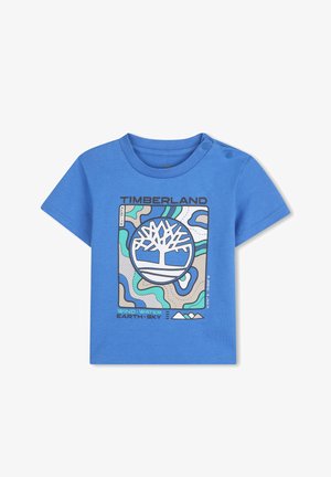 T-shirt en coton bleu arborant un design graphique avec le logo Timberland, des formes abstraites en vert et beige, et des fermetures à pression à l'épaule.