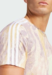 Kurzarm-T-Shirt mit einem marmorierten Muster in Lila und Gold, mit weißen horizontalen Streifen auf den Schultern und einem strukturierten Stoff.