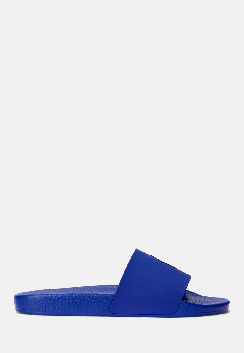 Sandale slide bleue avec semelle texturée et bride large, montrée de profil sur un fond clair uni.