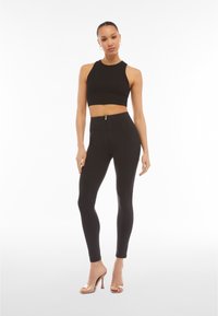 Crop top nero con design aderente, abbinato a leggings neri a vita alta con chiusura con zip e texture liscia. Sandali con tacco trasparenti.