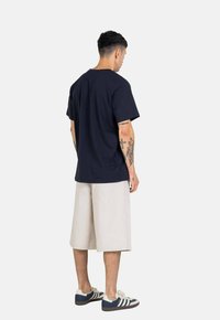 Navy cotton t-shirt, short sleeves, relaxed fit, paired with beige knee-length shorts, and navy sneakers with white stripes.