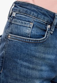 Jean en denim bleu ajusté avec une taille mi-haute, un design à cinq poches, des coutures ton sur ton et une petite étiquette de marque sur la ceinture arrière.
