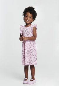 Vestido rosa con lunares y mangas con volantes, hecho de una tela suave. Combinado con zapatos morados claros que presentan un detalle de hebilla.