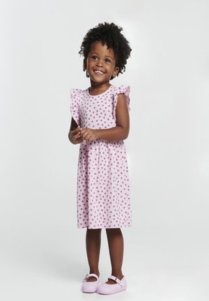 Vestido rosa con lunares y mangas con volantes, hecho de una tela suave. Combinado con zapatos morados claros que presentan un detalle de hebilla.