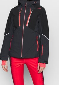 Zwarte skijas met contrasterende rode accenten, ritszakken en een capuchon. Gemaakt van gestructureerd, geïsoleerd materiaal voor warmte.